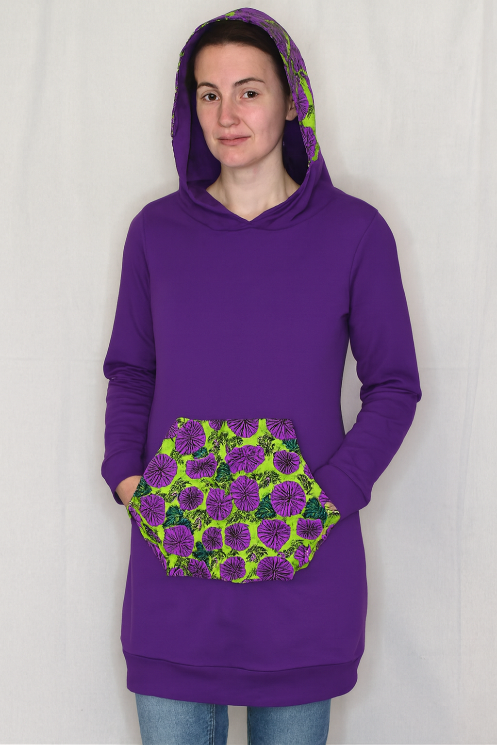 Person wearing a purple hoodie with a floral pattern on the pocket against a white background